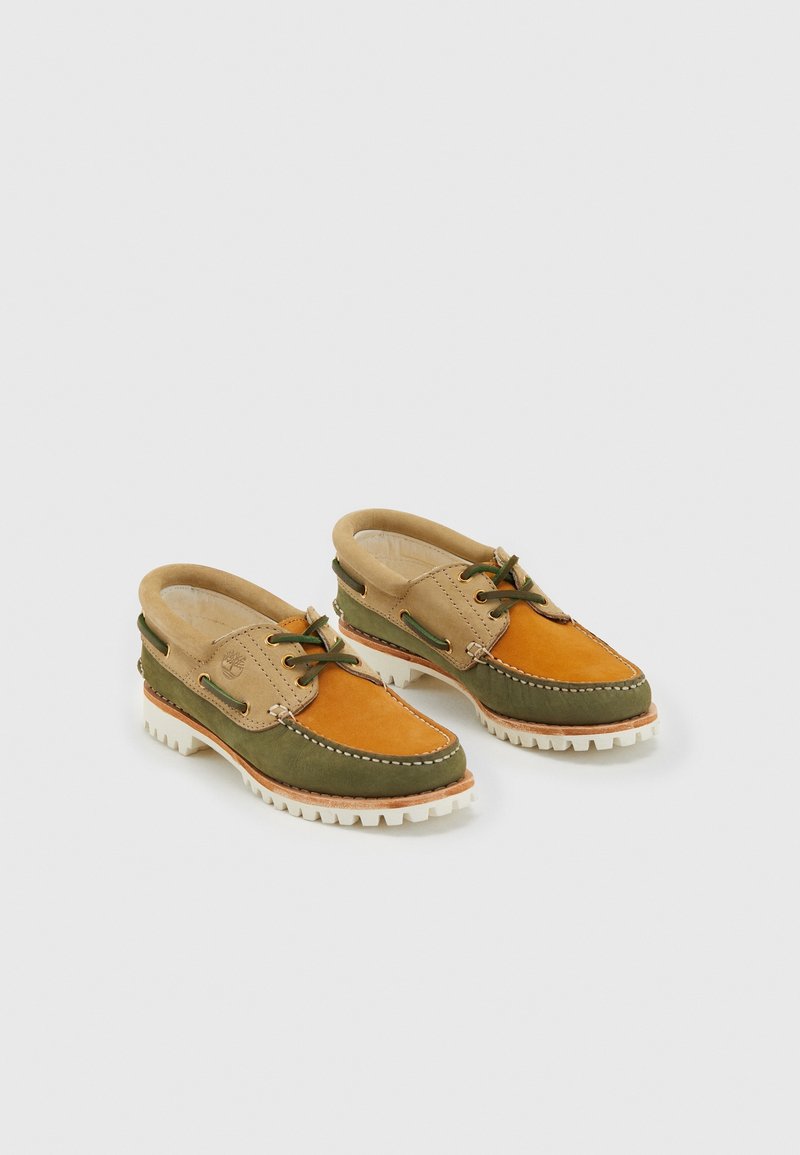 Chaussures bateau en cuir bicolore vert, beige et orange avec semelles blanches rugueuses et détails lacés sur fond uni.