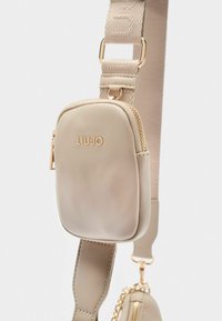 Borsa a tracolla in pelle beige con hardware dorato; presenta un compartimento con zip e una tracolla regolabile a fantasia. Logo Liujo impresso.
