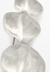 Silver metal earring featuring a three-leaf shape with textured surfaces. The design is smooth with rounded edges and a subtle shine.