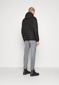 Veste matelassée noire avec coutures horizontales et capuche, associée à un jean gris clair et des bottines noires, vue de dos.