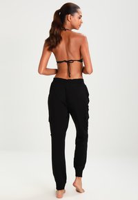 Schwarze Cargo-Hosen mit hochgekrempelten Knöcheln, seitlichen Taschen und einer lässigen Passform, kombiniert mit einem passenden Bikinitop im Halterneck-Stil.