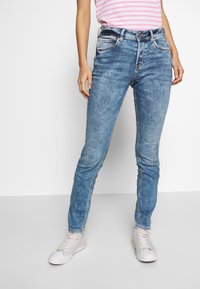 Ljusblå skinny jeans med urblekta områden, fem fickor och knappstängning. I kombination med vita högskurna sneakers.