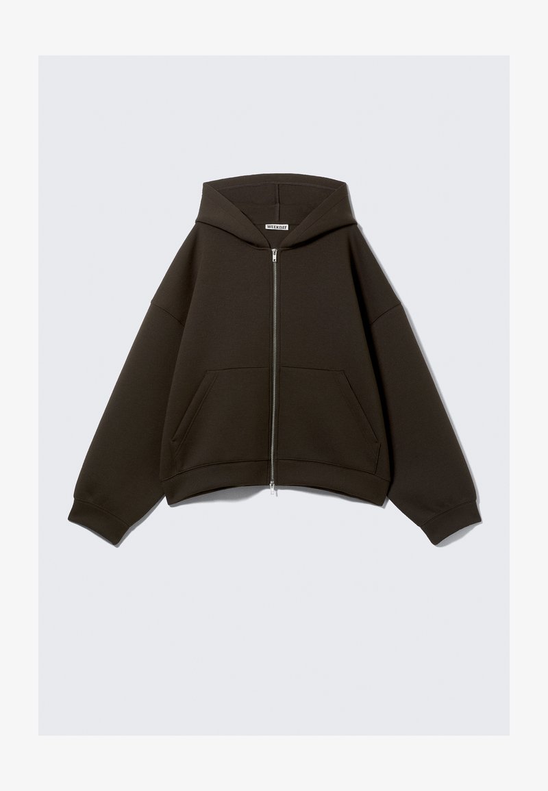 Sweat à capuche zippé marron foncé avec une capuche spacieuse, des épaules tombantes et deux poches avant. Confectionné dans un textile doux avec des poignets côtelés.