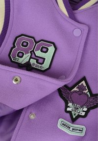 Purple fleece varsity jacket featuring embroidered patches, including number "89" and a heart with wings design. Silver snap buttons.