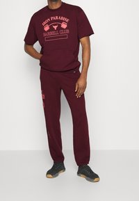 Conjunto deportivo burdeos que incluye una camiseta de manga corta con estampado gráfico y pantalones a juego. Fabricado en tejido suave, con un corte relajado.