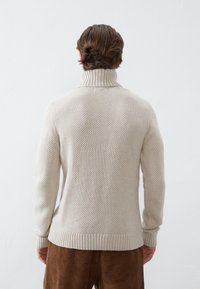 Light beige knitted sweater with a high collar, ribbed cuffs, and hem; textured pattern and smooth finish. Worn with brown corduroy pants.