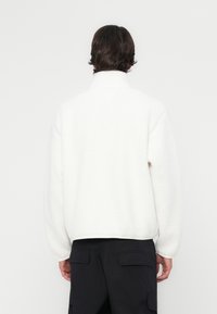 White fleece pullover with a high collar, relaxed fit, and ribbed hem. The texture is soft, featuring long, fluffy fibers.