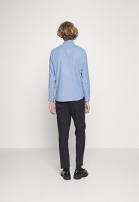 Ljust blå knapp-up skjorta med långa ärmar, subtil textur, rundad fåll, tillsammans med mörka skräddarsydda byxor och svarta skor.