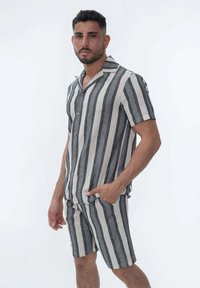 Chemise à manches courtes avec col et shorts assortis dans un motif rayé noir et crème. Fabriqué en tissu léger avec des boutons.