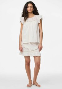 Top in cotone bianco con maniche arricciate e dettagli in pizzo, abbinato a una gonna arricciata coordinata. Entrambi hanno una consistenza liscia e una vestibilità rilassata.