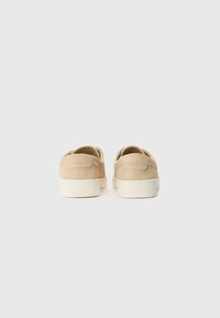 Beige velúr slip-on cipők texturált felülettel, fehér gumitalppal és logóval a sarkon. Minimalista dizájn, lekerekített élekkel.