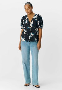 Blusa negra con estampado abstracto azul y blanco, mangas cortas abullonadas y escote en V. Combinada con jeans rectos de un azul claro.