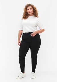 Svarta slim fit jeans med hög midja, tillverkade av elastisk denim. Kombineras med en figurformad vit t-shirt och vita sneakers.