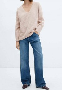 Lichtroze v-hals trui in een zachte brei, gecombineerd met blauwe wijde spijkerbroek en bruine schoenen. De outfit heeft een ontspannen pasvorm en een eenvoudig ontwerp.