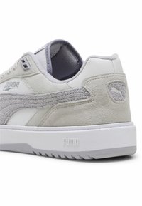 Zapatilla blanca y gris con un panel lateral de ante texturizado, acentos de cuero suave, cuello acolchado y suela de goma con el logo de Puma.