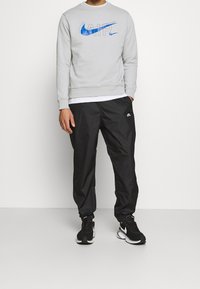 Grå sweatshirt med blå Nike-logga, tillsammans med svarta, lätta träningsbyxor med en liten logga, och svarta sportskor.