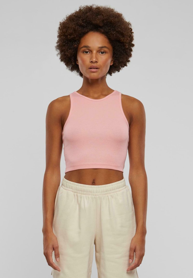 Hellpink, figurbetontes Crop-Top aus dehnbarem Baumwollmaterial mit rundem Ausschnitt und ärmellosem Design, kombiniert mit lässigen cremefarbenen Hosen.