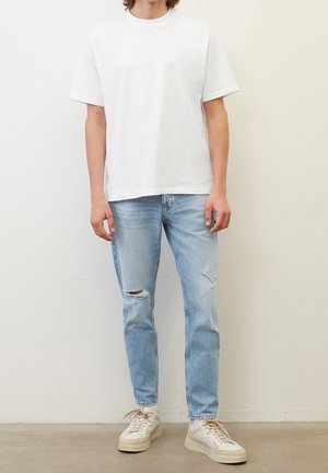 Camiseta blanca de algodón, corte relajado, combinada con jeans claros desgastados. Las zapatillas tienen acentos beige y una suela texturizada.