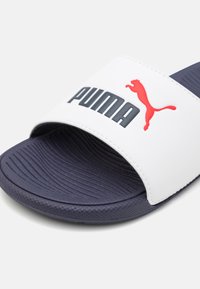 PUMA Riemensandale mit einem weißen synthetischen Obermaterial, einem auffälligen Logo, einer navyblauen Außensohle, einem strukturierten Fußbett und einem offenen Zehendesign.