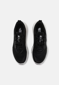 Chaussures de sport noires avec une tige en maille, des accents texturés et une semelle blanche. Dispose d'un système de laçage et d'un logo sur la languette.