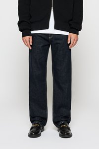Donkerblauwe denim jeans met een recht gesneden pasvorm, gecombineerd met een zwarte gebreide rits-vest en glanzende zwarte loafers met gouden accenten.