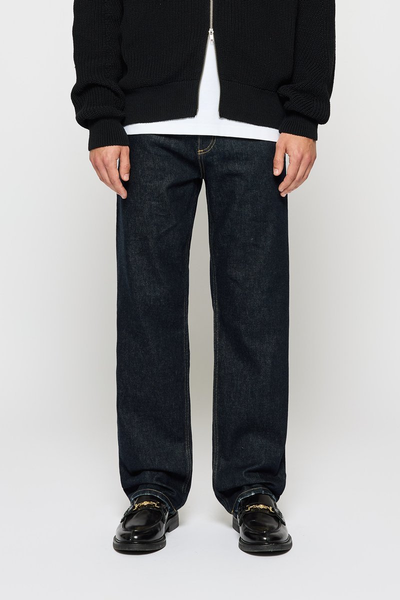 Donkerblauwe denim jeans met een recht gesneden pasvorm, gecombineerd met een zwarte gebreide rits-vest en glanzende zwarte loafers met gouden accenten.