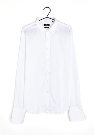 Camicia bianca a maniche lunghe con bottoni, realizzata in un tessuto morbido, caratterizzata da un colletto classico, bottoni frontali e polsini ampi. Appesa a un gancio nero.