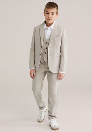 Helehall kolmekohaline ülikond, mis koosneb jopest, vestist ja pükstest, millel on sile tekstuur ja pruuni värvi nööbid, sobitatud valgete tennistega.