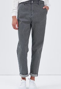 Randiga byxor med avslappnad passform, med svarta och vita vertikala ränder, vänd upp ärmar och framfickor, som bärs med vita sneakers.