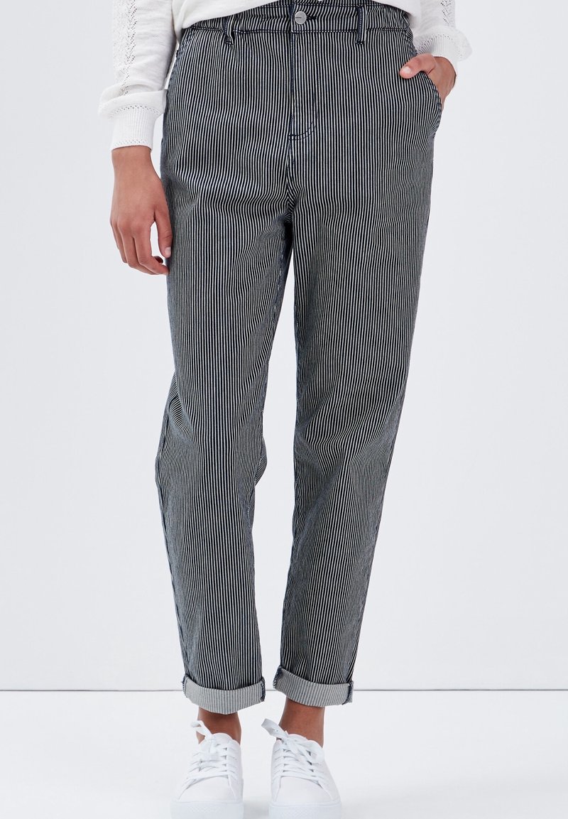 Randiga byxor med avslappnad passform, med svarta och vita vertikala ränder, vänd upp ärmar och framfickor, som bärs med vita sneakers.