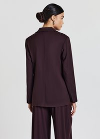 Blazer personalizzato bordeaux con colletto a nuoce, apertura sul retro singola e maniche lunghe, realizzato in un tessuto liscio di peso medio.