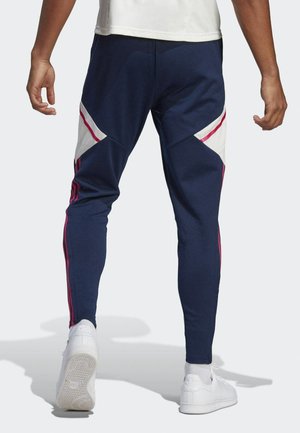 Marine joggers met witte en roze diagonale accenten. Strakke pasvorm, rekbare stof, met zijstrepen en taps toelopende benen. Witte sneakers zichtbaar.