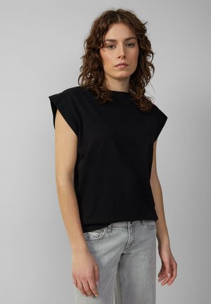 Schwarzes Baumwoll-T-Shirt mit kurzen, strukturierten Ärmeln und rundem Ausschnitt, kombiniert mit hellgrauen Jeans, die einen lässigen Look zeigen.