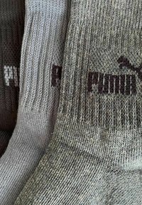 Zwei Paar gestrickte Socken, ein hellgraues und ein dunkelgraues, mit einem braunen Logo. Die Textur ist weich und hat ein geripptes Muster.