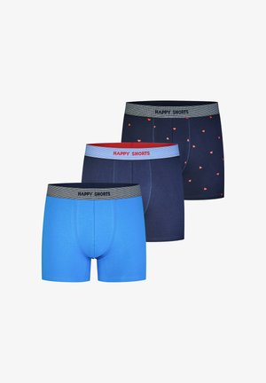 Lächelnder, oberkörperfreier Mann mit tribal Tätowierung am Arm trägt marineblaue Boxershorts mit kleinen roten Herzen und grauem Bund mit der Aufschrift "HAPPY SHORTS."