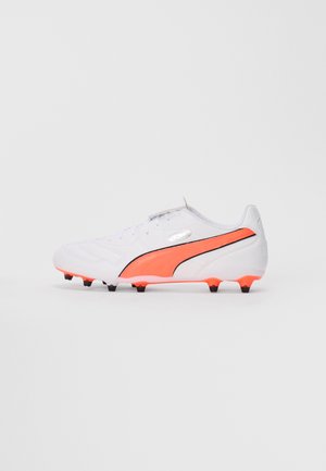 Crampons de soccer blancs avec une bande orange vif et noire, des crampons noirs et une sangle en velcro sur un fond uni.