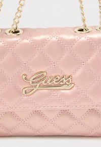 Ροζ καπιτονέ γυναικεία τσάντα με χρυσό μεταλλικό λογότυπο Guess και λουράκια από αλυσίδα. Η επιφάνεια έχει γυαλιστερό φινίρισμα με ραμμένα διαμαντένια σχέδια.