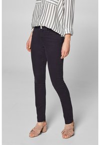 Jeans ajustados de mezclilla oscura con una textura suave, combinados con una camisa de manga larga a rayas. El conjunto incluye calzado de color claro.