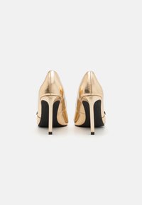 Gold metallic high-heeled shoes with a sleek design, pointed toe, and black soles. The heels are narrow and stiletto-style for added height.