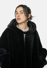 Veste à capuche en fourrure noire avec une fermeture éclair brillante, design oversize et texture douce. Elle présente une finition pelucheuse et de grandes manches arrondies.