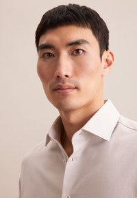 Lange mouwen lichtbeige overhemd met een geweven textuur, button-down kraag en subtiele glans. Beschikt over twee knopen en een standaard pasvorm.