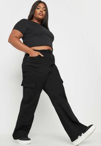 Svart kort topp och cargobyxor med sidofickor, med en rak ben-design och strukturerad tyg. Bärs med svarta och vita sneakers.