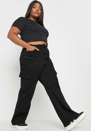Top corto nero e pantaloni cargo con tasche laterali, caratterizzati da un design a gamba dritta e tessuto testurizzato. Indossati con sneaker nere e bianche.