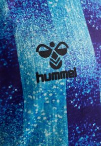 Sort styliseret bi-logo over teksten "hummel" på blå tekstureret stof med lyseblå og mørkeblå lodrette striber.