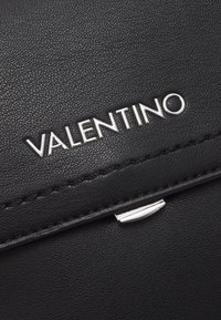 Black leather wallet featuring silver "VALENTINO" logo, stitched accents, and a smooth texture with a metal snap closure.