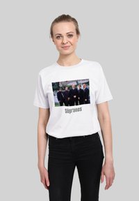 Bílá bavlněná trička s grafickým potiskem šesti mužů v oblecích. Pod ním je text "The Sopranos." Standardní kulatý výstřih a krátké rukávy.