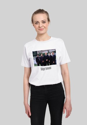 Hvid bomulds t-shirt med et grafisk print af seks mænd i jakkesæt. Teksten nedenfor lyder "The Sopranos." Standard rund hals og korte ærmer.