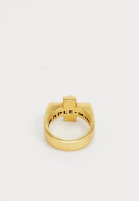 Kuldne metallring, millel on tasane ülemine osa ja rist-aksent. Siseruumis on graveeritud "MAPLE•SILVER." Sile, matt viimistlus. Ümmargune kuju.