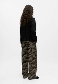 Schwarzer Sweatshirt mit einem kurzen Design, kombiniert mit weiten braunen Hosen, die ein schwarzes Tigerstreifenmuster aufweisen. Glatte Textur und lockerer Schnitt.