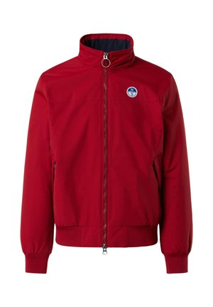 Giacca bomber rossa con colletto alto, chiusura a zip frontale, tasche laterali e polsini a costine. Presenta una patch rotonda blu sul lato sinistro del petto.